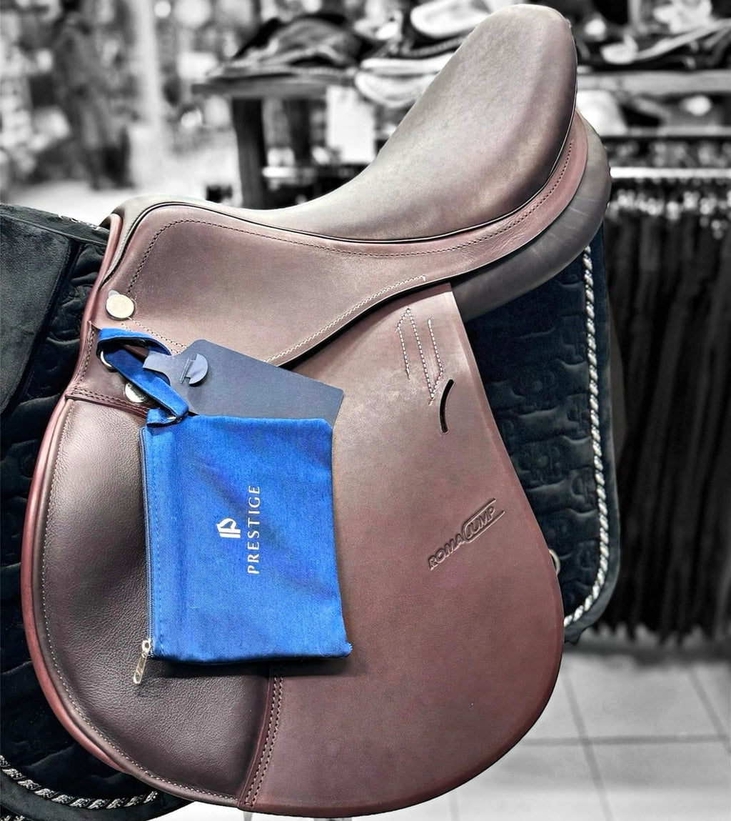 Brown leather saddle with a blue tag featuring 'Prestige' branding in an indoor setting.